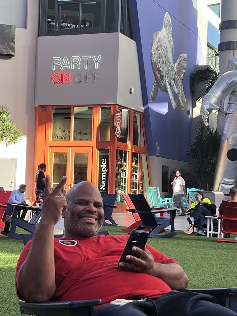 Tamika Felder's husband, Rocky, smiling and pointing at a sign behind him that reads "Party On," celebrating his birthday in Puerto Rico.