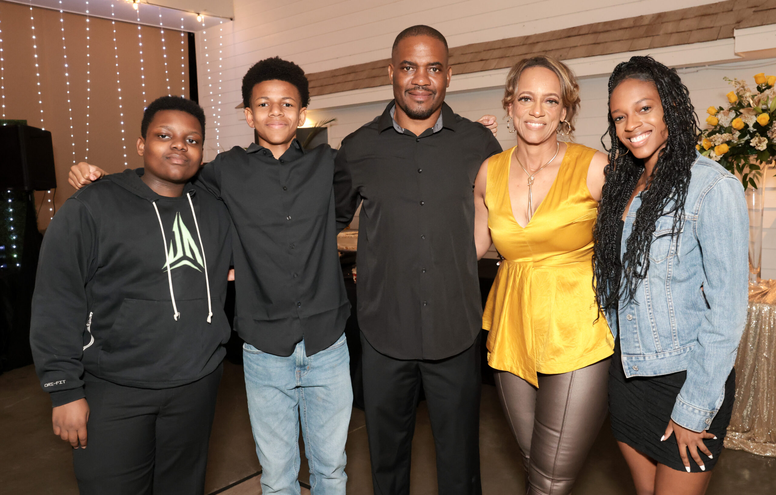 Quan Myers stands with her family at her surprise 50th birthday party, smiling alongside her husband, Derrick, and their children—Colin (12), Tyson (16), and Kennedy (19).