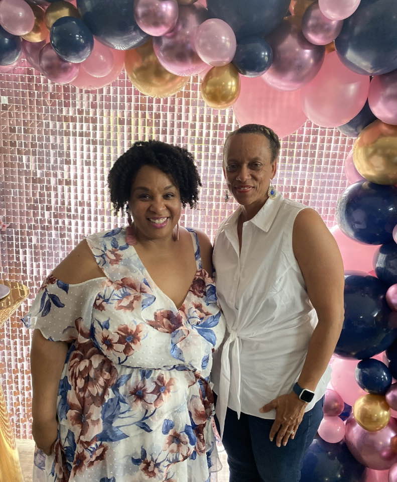 Tamika Felder and her best friend Quan Myers stand together at a party in front of a colorful balloon arch, smiling warmly at the camera.