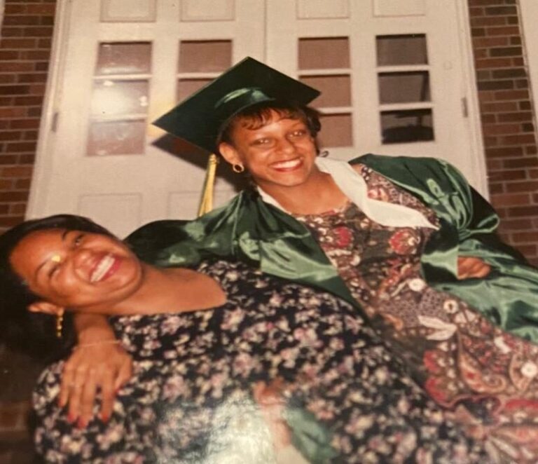 Tamika Felder and her best friend Quan Myers pose together at their high school graduation. Quan wears a green gown and mortarboard, while Tamika leans back, smiling widely as they hold onto each other.