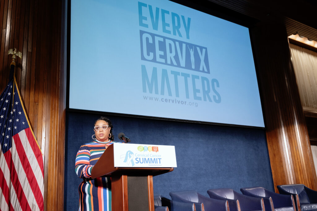 Tamika Felder, founder of Cervivor, delivers her opening State of Cervical Cancer address at the 2025 Cervical Cancer Summit, standing at a podium in front of a large screen that reads “Every Cervix Matters.”